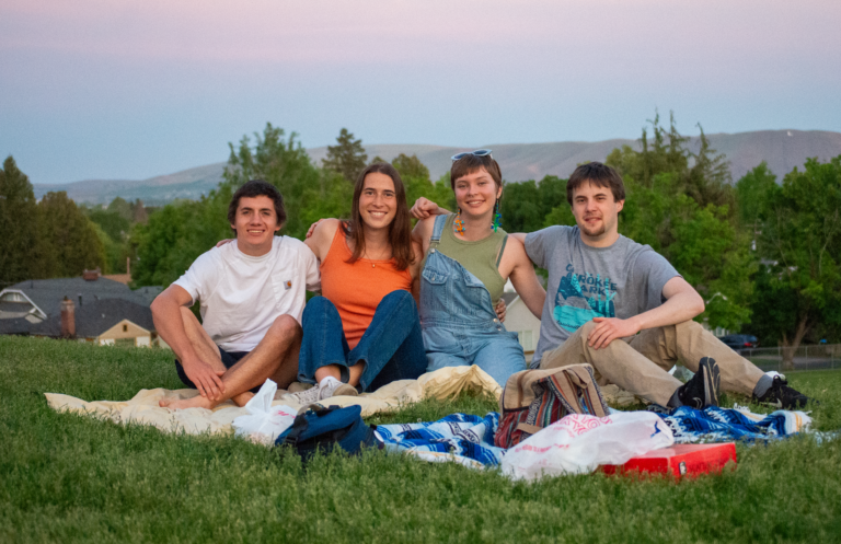 four Jesuit Volunteers with arms around each other in front of a sunset over the hills in Yakima