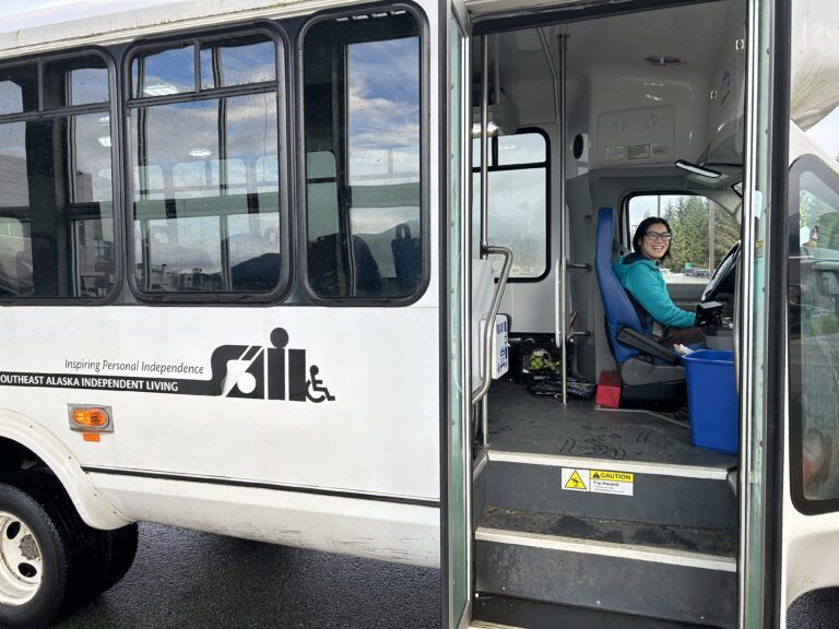 Julia driving a white bus with the SAIL logo on the side.