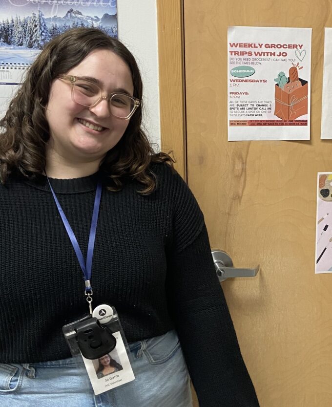 Jesuit Volunteer smiling by fliers wearing nametag for office while at service